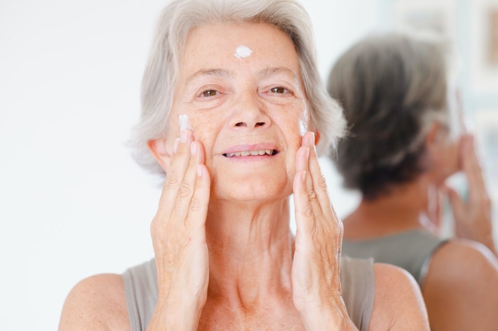 Forehead Wrinkles. Portrait of senior beautiful gray-haired woman applies anti aging cream on wrinkled face