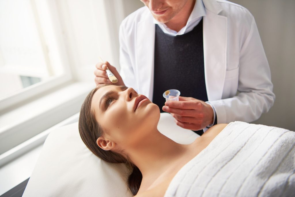 Myth Busting Young cosmetologist putting mask on woman in salon